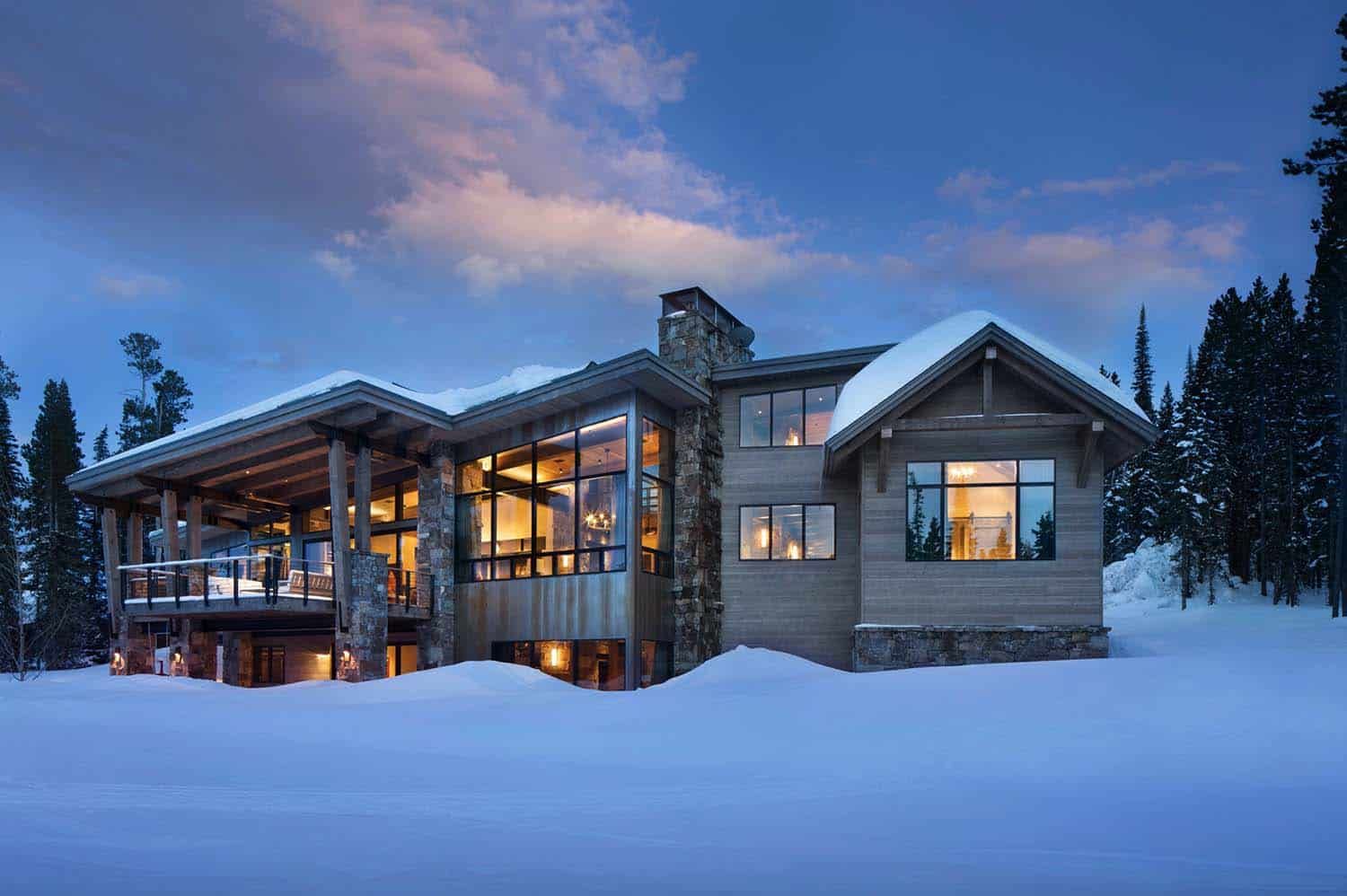 a mountain home at dusk with snow outside and warm lights glowing inside