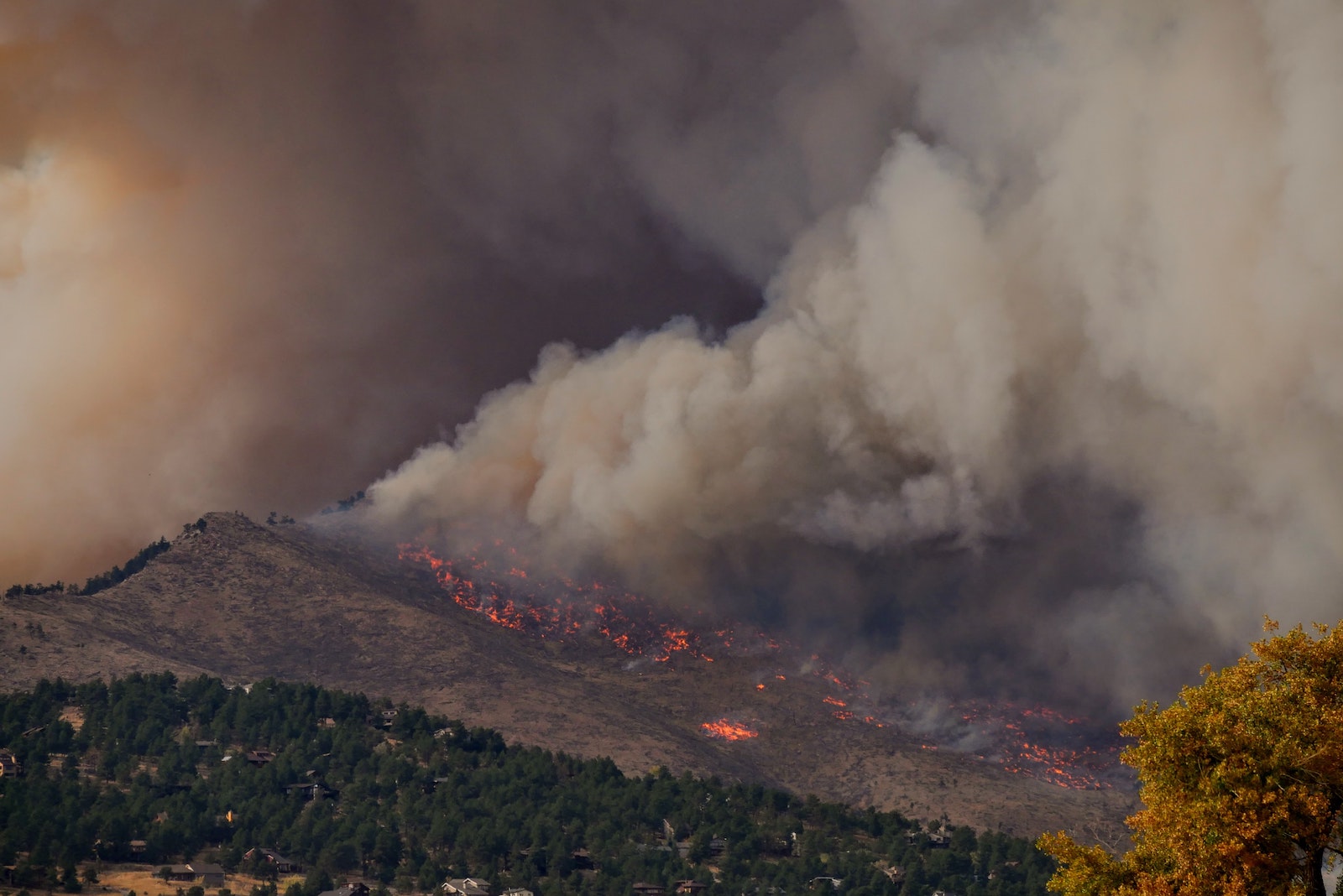 wildfire in the mountains with large smoke cloud billowing from it